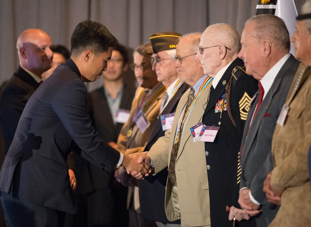 photo of Consul General Jimin Kim shaking hands with a line of veterans